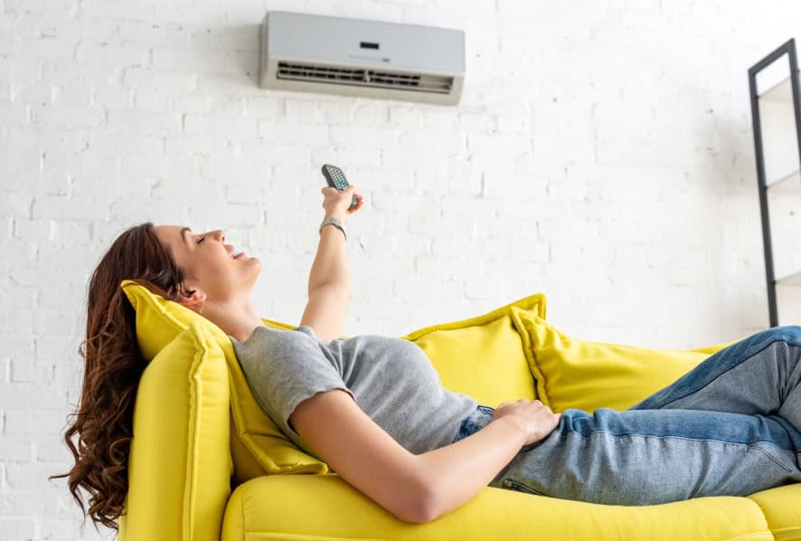 women laying on yellow couch with remote controlling new ac unit